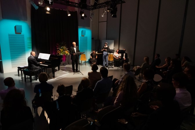 Photo of the accessible concert with aview of audience members then the spotlit stage where the tenor and pianist are performing.