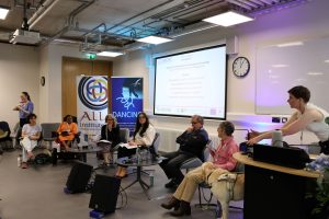 Third roundtable of the conference, featuring the chair and their guide dog, a member of the DANCING team helping to set up, the five speakers, and Irish Sign Language Interpretation.